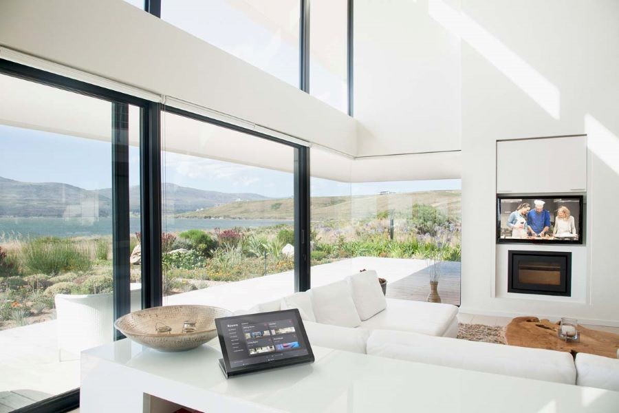 A home’s living area overlooking the ocean with a home automation touchscreen on a counter and a TV behind a raised panel.