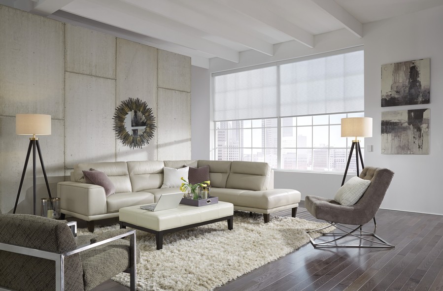 A modern living room with a cream leather sectional, cozy rug, large windows with sheer motorized blinds, and contemporary décor like floor lamps and wall art.