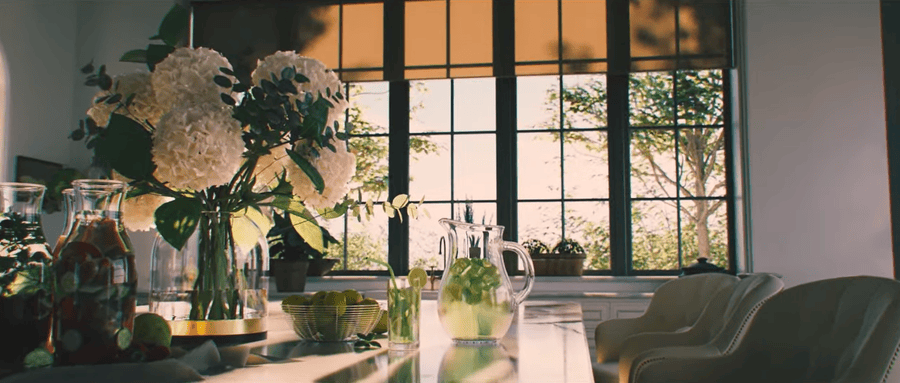 Bright and elegant kitchen with large windows featuring Lutron motorized shades, a vase of white flowers, and a table adorned with pitchers of infused water and fruit.