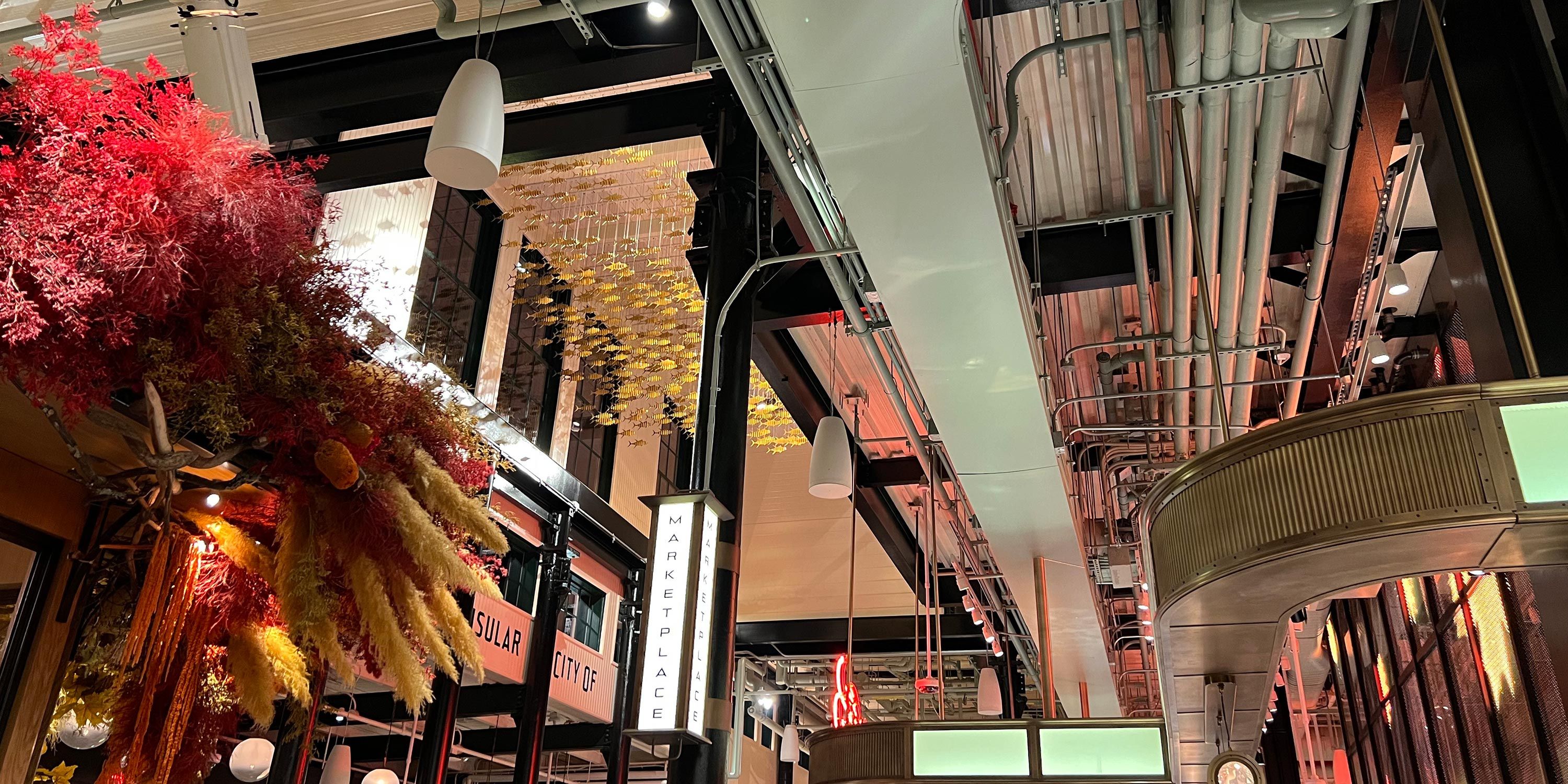 Interior of a modern marketplace with industrial design elements and vibrant floral decorations hanging from the ceiling.