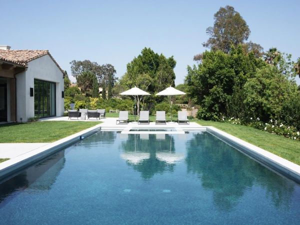 Luxurious backyard pool with lounge chairs and umbrellas, set in a well-manicured lawn with a backdrop of trees and greenery.