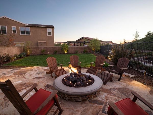 Backyard fire pit area with Adirondack chairs, set on a stone patio with a view of the lawn and garden, perfect for evening gatherings.