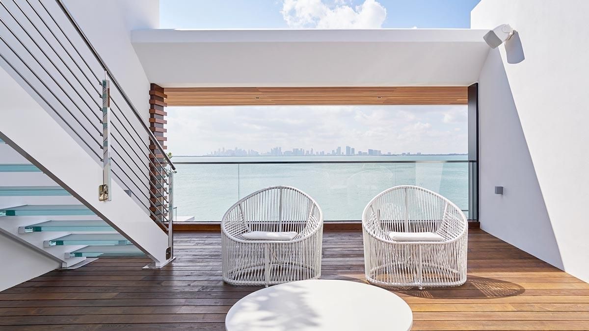 Minimalist outdoor deck with two white chairs and a stunning ocean view, featuring a Sonance marine speaker on the wall.