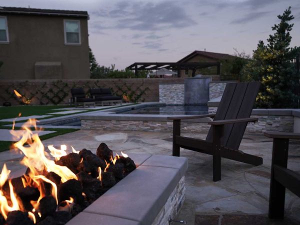 Cozy backyard scene with a fire pit and Adirondack chairs, set against a modern home with a pool and lush greenery.