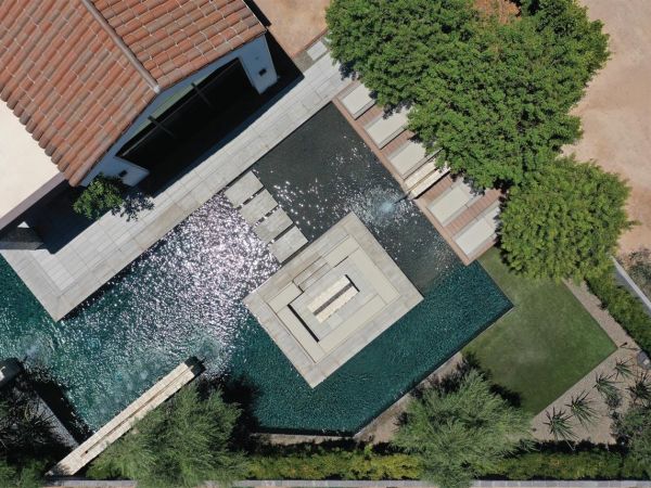 Aerial view of a modern home with a unique geometric pool design, surrounded by lush landscaping and outdoor seating areas.